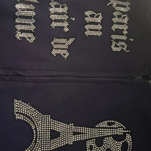 Mörkblå hoodie med strass och tryck - Mörkblå hoodie från BLINGLUCID med huva och dragkedja. Framsidan har coolt strasstryck med texten 'paris en clair de lune' och motiv av Eiffeltornet och månen. Tillverkad i mjuk bomulls- och polyestermix. Perfekt för dig som gillar statement-plagg.