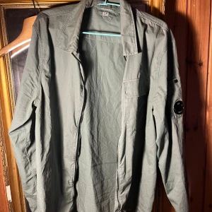 Grön overshirt från C.P. Company L - Snygg grön overshirt från C.P. Company i bomull med klassisk krage, dragkedja. Perfekt lager-på-lager-plagg, passar dig som gillar streetwear och italiensk design. Skick: 8/10, säljer pågrund av att den är för liten, den är äkta