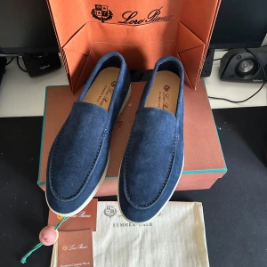 Mörkblå mockaloafers från Loro Piana - Snygga loafers från Loro Piana i mörkblå mocka med vit sula. Skorna har en klassisk och stilren design med rund tå och diskreta sömmar. Perfekta för dig som vill ha en clean och lyxig look till sommaren.