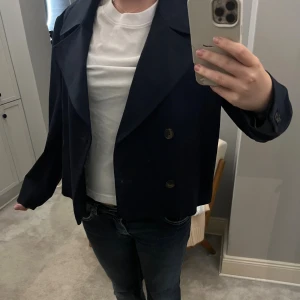 Mörkblå kort trenchcoat från Zara - Aldrig använd snygg mörkblå skepparkavaj från Zara med dubbelknäppning och bred krage. Jackan har en croppad passform, långa ärmar och två framfickor. Perfekt för dig som gillar klassisk stil med modern twist.