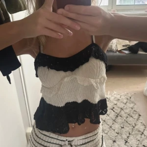 Svartvit stickad linnetopp med volang - Säljer en söt stickad linnetopp i svart och vitt med volangdetaljer. Toppen är croppad och har tunna axelband, perfekt för dig som gillar en trendig och lekfull stil. Materialet är mjukt och luftigt, och volangerna ger en extra touch till looken.