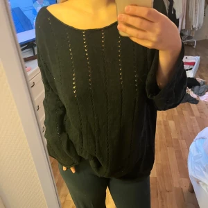 Svart stickad tröja med hålmönster - Mysig svart stickad tröja med bred halsringning och diskret hålmönster i vertikala rader. Tröjan har långa, lite vidare ärmar och en loose passform som ger en avslappnad vibe. Perfekt att slänga på sig när det är lite kyligare ute.