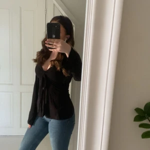 Svart omlottopp från Design by Si - Supersnygg svart omlottopp från Design by Si med långa ärmar och knyt framtill. 