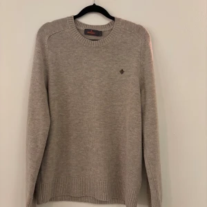 Beige stickad tröja från Morris - Beige stickad tröja från Morris med rund halsringning och diskret logga broderad på bröstet. Tröjan har ribbade muddar vid ärmslut och nederkant, och är perfekt för lager-på-lager under kyliga dagar. Den är använd 1 gång. Nypris 1899