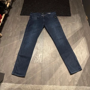 Replay Anbass jeans mörkblå 30/30 - Snygga mörkblå Replay Anbass jeans i klassisk femficksmodell. Jeansen har en slim passform med raka ben och är tillverkade i mjukt jeansmaterial. Perfekt för dig som gillar stilrena och moderna jeans med diskreta detaljer.