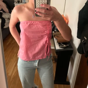 Rosa bandeau tubtopp med knyt - Säljer en rosa bandeau tubtopp i tunn bomull med snygg knytning och slits på sidan. Toppen är ärmlös och har en luftig, loose passform som passar perfekt till jeans eller kjol. Aldrig använd 