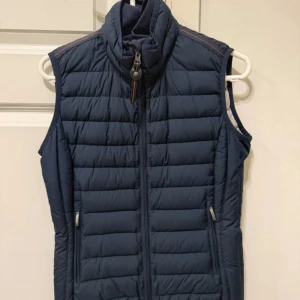 Parajumper väst  - Parajumper dunväst med quiltad design och hög krage. Västen har en hel dragkedja framtill och två sidofickor med dragkedja. Perfekt att slänga över en hoodie eller långärmad tröja för extra värme. Enkel och stilren look som funkar till det mesta.