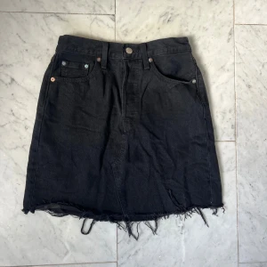 Svart jeanskjol från Levi's med fransad kant - Svart jeanskjol från Levi's Kjolen har en rak passform och är i en kort modell. 