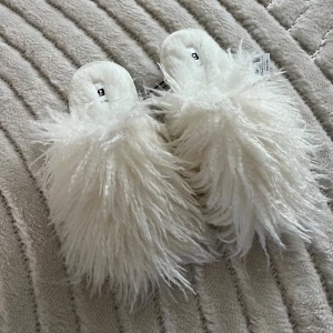 Fluffiga vita tofflor från Gina Tricot - Supermjuka och fluffiga tofflor från Gina Tricot i vit färg. De har en öppen tå och är täckta av långhårig pälsimitation som ger en riktigt statement-look. Perfekta för dig som vill sticka ut och ha något extra mysigt på fötterna. Helt nya med prislapp🩷