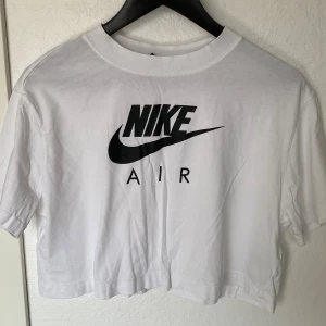 Vit croppad Nike Air t-shirt - Säljer en vit croppad t-shirt från Nike med klassisk svart Nike Air-logga framtill. T-shirten har rund halsringning och korta ärmar. Tillverkad i mjuk bomull, perfekt för en sportig och avslappnad stil.