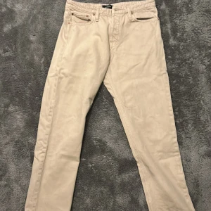 Beige jeans från Jack & Jones - Snygga beige jeans från Jack & Jones med klassisk femficksdesign och raka ben. Byxorna är tillverkade i bomull och har en stilren look med läderpatch bak i midjan. Perfekta för dig som gillar en enkel och clean stil.