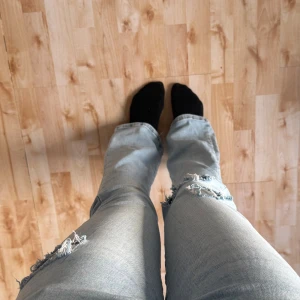 Ljusblå flare jeans från Never denim - Säljer ett par ljusblå jeans från Never Denim med låg midja och flare-ben. Jeansen har slitna detaljer och hål på ena benet för en cool, avslappnad vibe. Perfekt för dig som gillar trendiga och bekväma jeans med lite edge.