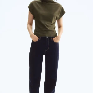 Olivgrön tuntstickad topp med kort ärm - Snygg olivgrön stickad topp med korta ärmar och hög hals. Modellen är rak och något croppad med bred ribbad kant nedtill. Perfekt att styla med jeans eller kjol för en clean look. Använd 1 gång💕