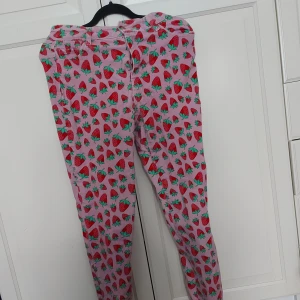 Rosa jordgubbsmönstrade jeans från Sugar Thrillz - ⚠️ Skriv till mig innan köp!⚠️Superfina jeans från Sugar Thrillz i storlek S, med ett lekfullt jordgubbsmönster på rosa bakgrund. Byxorna har klassisk femficksdesign, bälteshällor och stängs med dragkedja och knapp. Perfekt för dig som vill sticka ut med färg och mönster.