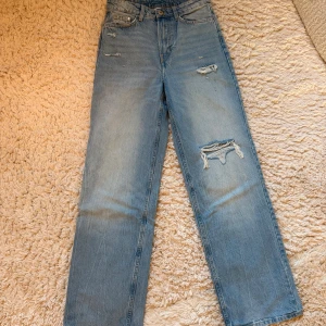 Ljusblå slitna raka jeans - Ljusblå jeans med raka ben och flera slitningar på låret och knät. Klassisk femficksmodell med hög midja och dragkedja. Perfekta för dig som gillar en trendig och bekväm stil.