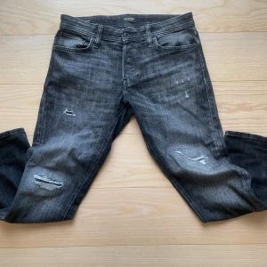 Jack & Jones jeans med slitningar - Säljer ett par helt nya tvär feta Jack & Jones jeans med slitningar. Jeansen är mörkgrå och har en tvär fet tvätt. Storlek 30/30. Vid fler frågor och funderingar är de bara att höra av sig 