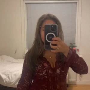 Vinröd spetsblus med v-ringning - Säljer en vinröd blus i spets med v-ringad hals och utsvängda ärmar. Blusen är genombruten med blommigt spetsmönster och har en figurnära passform. Perfekt för dig som vill ha en snygg och trendig topp med fina detaljer. Kan användas till fest, jobba, skola och allmänt vardag. ❣️