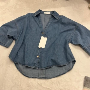 Blå jeansskjorta med v-ringning - Snygg blå jeansskjorta med trekvartsärmar från Zara. Aldrig använd, säljer då jag aldrig fått tillfälle att använda den