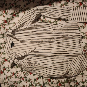 Vit randig skjorta från H&M - Vit skjorta från H&M med svarta tunna ränder. Klassisk krage, långa ärmar och knäppning framtill med vita knappar. Tillverkad i mjuk bomull, perfekt för en clean och stilren look.