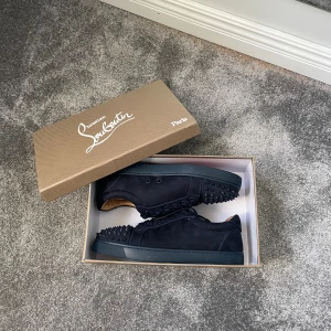 Christian Louboutin Louis Strass sneakers - Säljer ett par mörkblå Christian Louboutin Louis Strass sneakers i mocka med coola nitar framtill och den ikoniska röda sulan. Skorna har snörning och en lyxig känsla med läderdetaljer på insidan. Perfekta för dig som vill sticka ut med exklusiv streetstyle.