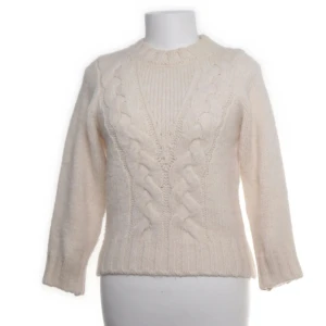 Vit stickad tröja med flätmönster - Mysig vit stickad tröja med klassiskt flätmönster framtill och ribbade muddar. Tröjan har rund halsringning och långa ärmar, perfekt för kyliga dagar. Den är enkel att matcha och ger en clean och stilren look.