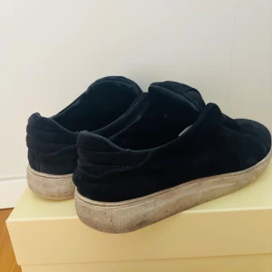 Mörk blå Axel Arigato opens - Svarta slip-on sneakers från Axel Arigato i mocka med vit, platt sula. Snygg minimalistisk design utan snörning och med diskret branding på sulan. Skorna har liten slitage och kommer med originalkartong och dustbag.