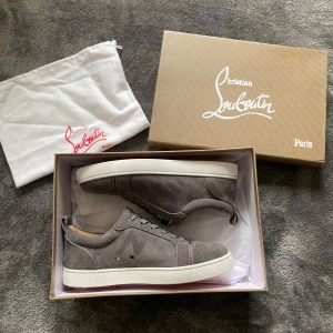 Grå Christian Louboutin skor  - Snygga grå sneakers i mocka från Christian Louboutin med klassisk röd sula. Skorna har rund tå, snörning och vit platt sula. Insidan är fodrad i beige läder och detaljerna är stilrena. Perfekta för dig som vill ha något exklusivt och stilrent. Som du ser även på bilden så är mockan väldigt bra och inte sliten skorna har bara använts 2 gånger 