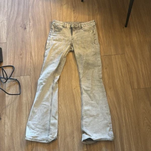 Grå bootcut jeans med slitna detaljer - Grå jeans med bootcut passform och klassisk femficksdesign. Jeansen har låg midja och är tillverkade i mjukt denimtyg. Lite slitna längst ner, två små blåa färg fläckar