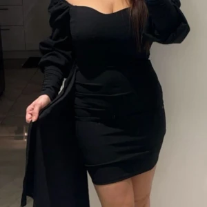 Svart kort klänning med puffärm - Supersnygg svart kort klänning med figurnära passform och puffiga långa ärmar. Offshoulder-modell som ger en trendig och elegant look. Perfekt för dig som vill sticka ut och känna dig extra fin.
