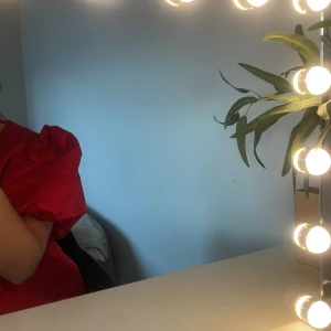 Röd blus med puffiga ärmar!! - Supersnygg röd  blus med stora puffärmar och djup v-ringning. Klänningen har en markerad midja med knyt framtill och är gjord i ett glansigt satinliknande material. Perfekt för dig som vill sticka ut och älskar statement-ärmar! Från Nelly aldrig använd!!