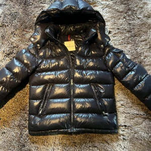 Moncler Maya - Snygg svart pufferjacka från Moncler med glansig finish, huva och dragkedjor framtill. Jackan har Moncler-logga på ärmen och är modellen New Maya, storlek 164 men den passar som en helt Vanlig 1/S. Jackan är Äkta men det tillkommer tyvärr inget kvitto (vid fler bilder är det bara skriva)✍️jackan är i väldigt fint skick och Nypriset ligger på 8000kr ✅