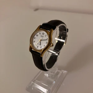 Casio LTP-1154 klassisk armbandsklocka - Stilren Casio LTP-1154 armbandsklocka med rund vit urtavla, svarta siffror och guldfärgat boett. Klockan har ett brunt läderband och detaljer i guld. Baksidan är i rostfritt stål och modellen är vattenresistent. Perfekt för dig som gillar klassisk och tidlös design. Behöver ett nytt batteri.