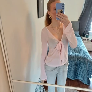 Ljusrosa roset topp från Gina Tricot - Säljer en ljusrosa roset topp från Gina Tricot i storlek M. Toppen har lång ärm, v-ringning och knyt framtill som ger en snygg och feminin look. Materialet är tunt och mjukt, perfekt för att skapa en chill och trendig outfit. Men ser lite igenom som ni kanske ser. Jag säljer den är lite för stor 