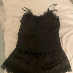 Svart spetspyjamas  - Säljer en svart spets pyjamas   och fina spetsdetaljer längs urringningen. Pyjamasen  har en mjuk och följsam känsla, perfekt för en chic och avslappnad look.