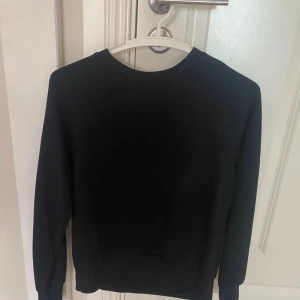 Svart basic tröja från H&M XS - Enkel svart långärmad tröja från H&M Basics i storlek XS. Tröjan har rund halsringning och är tillverkad i mjuk bomullsmix, perfekt för lager-på-lager eller som den är. Stilren och passar till allt.
