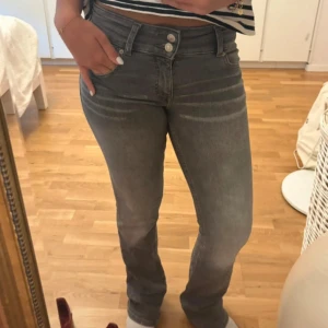 Gråa jeans från Bershka, bootcut - Gråa jeans från Bershka med bootcut. Jeansen har två knappar i midjan, klassiska fem fickor och lätt slitna detaljer vid benslut. Snygg tvätt och stretchigt material som sitter skönt.