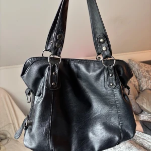 Svart väska - En svart rymlig väska med brunt innerfoder. Har 3 innerfickor varav en med dragkedja, den fickan har vid ett tillfälle spruckit i sömmen så det har jag lagat (se bild 5)👍Väskan stängs med dragkedja🥰