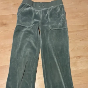 Mörk gröna Juicy Couture - Mysiga mörk gröna mjukisbyxor från Juicy Couture i velour med bred resår i midjan och stora fickor fram. Byxorna har broderad logga på ena fickan och bakfickor med knappar. Perfekta för chill eller streetwear.dock har jag haft en liten klick nagel lim på låret på byxan men hittade ej dem nu när jag tog bilderna.