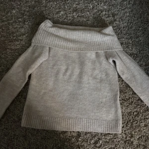 Beige offshoulder stickad tröja Gina Tricot - Supermysig beige stickad tröja från Gina Tricot med bred ribbad offshoulder-krage. Långärmad och perfekt för lager-på-lager under höst och vinter. Enkel att matcha med jeans eller kjol för en chill look.