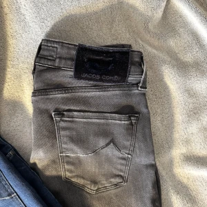 Svarta jeans från Jacob Cohen - Snygga svarta jeans från Jacob Cohen med diskret tvättad look och klassiska fem fickor. Jeansen har raka ben och normal passform, tillverkade i mjukt bomullsmaterial med stretch för extra komfort. Perfekta för dig som gillar stilrena och moderna jeans.