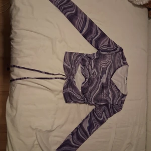 Lila mesh topp med vågigt mönster - Säljer en lila mesh topp från FB Sister i storlek XXS. Toppen har ett vågigt abstrakt mönster i olika lila nyanser, långa ärmar och knytband framtill. Materialet är tunt och stretchigt,och den är öppen vid magen💕