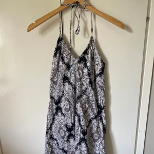 Svartvit mönstrad klänning  - Klänning i svart och vitt med paisleyinspirerat mönster. Klänningen har smala axelband som knyts i nacken och v-ringad hals. 