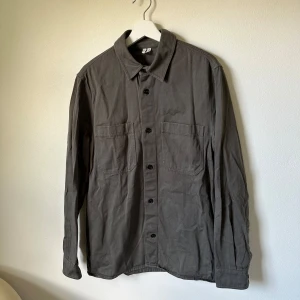 Grön overshirt från Arket, storlek 48 - Säljer en stilren grön overshirt från Arket i storlek 48. Skjortan har två stora bröstfickor, klassisk krage och knäppning framtill. Tillverkad i bomull och passar perfekt för lager-på-lager. Enkel och clean look som funkar till det mesta. 2I2