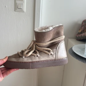 Beige skor från Inuikii - Säljer ett par beige vinterboots från Inuikii med högt skaft, grova snören och mjukt foder. Skorna är i mocka och skinn med en platt sula och rund tå. Perfekta för kalla dagar och riktigt snygga till vinterlooken. Super snygga. Pris kan diskuteras 