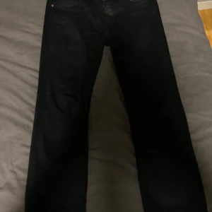 Svarta Levi's 501 jeans W29 L32 - Säljer ett par svarta Levi's 501 jeans i klassisk rak modell. Jeansen har fem fickor, mässingsfärgade nitar och Levi's Premium-märke på insidan. Tillverkade i slitstarkt jeanstyg och passar perfekt till en streetig look. Jeansen är lite urtvättade. Storleken är 29/32 men den är klippta till 29/30
