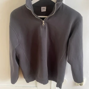 Mörkgrå half zip tröja från Zara - Mörkgrå sweatshirt från Zara med half zip-dragkedja och hög krage. Tröjan har lång ärm och en avslappnad passform, perfekt för lager-på-lager. Tillverkad i mjuk bomull för extra komfort.