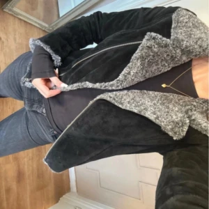 Svart mocka från Jofama, stl 36 - Säljer en svart mockajacka från Jofama i storlek 36. Jackan har grått fluffigt teddyfoder, bred krage och dragkedja framtill. Snygg och stilren modell med detaljer i silver och mjuk känsla, perfekt för kyliga dagar.