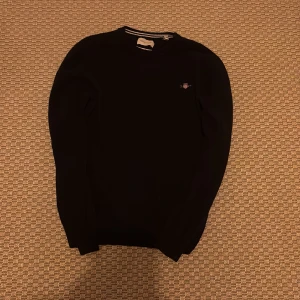 Svart lammullströja från Gant - Klassisk svart tröja från Gant i superfin lammull. Tröjan har rund halsringning, broderad Gant-logga på bröstet och ribbade muddar. Perfekt för dig som gillar stilrena och tidlösa plagg.