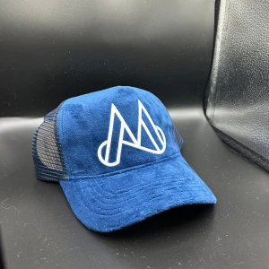 Blå mockakeps med vit M-logga - Snygg blå keps med framsida i mjuk mocka och mesh på sidorna. Stor vit broderad M-logga framtill ger en cool vibe. Perfekt för dig som gillar streetstyle och vill sticka ut. Justerbar baktill för bästa passform.