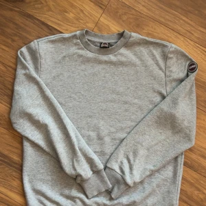 Grå sweatshirt från Colmar Originals - Snygg grå sweatshirt från Colmar Originals med rund hals och ribbade muddar. Tröjan har en clean look med Colmar-logga på ärmen och är tillverkad i mjuk bomullsmix. Perfekt för en chill och stilren vibe.